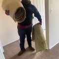 Bison Dump crew member carrying rolled carpet through a hallway during a Salem cleanout
